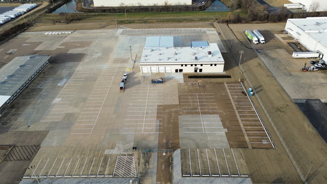 Aerial view of an industrial parking lot and building with organized vehicle spaces.