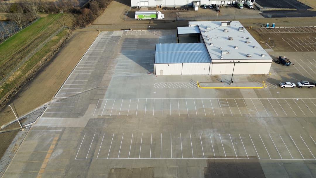 Aerial view of an empty commercial parking lot next to a warehouse and vehicles.