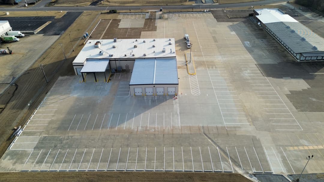 Aerial view of a large industrial building with an empty parking lot and surrounding area.