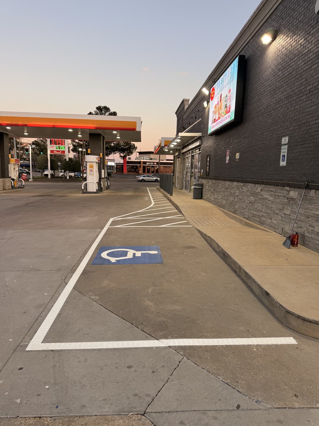 Gas station exterior with accessible parking and convenience store entrance at sunset.