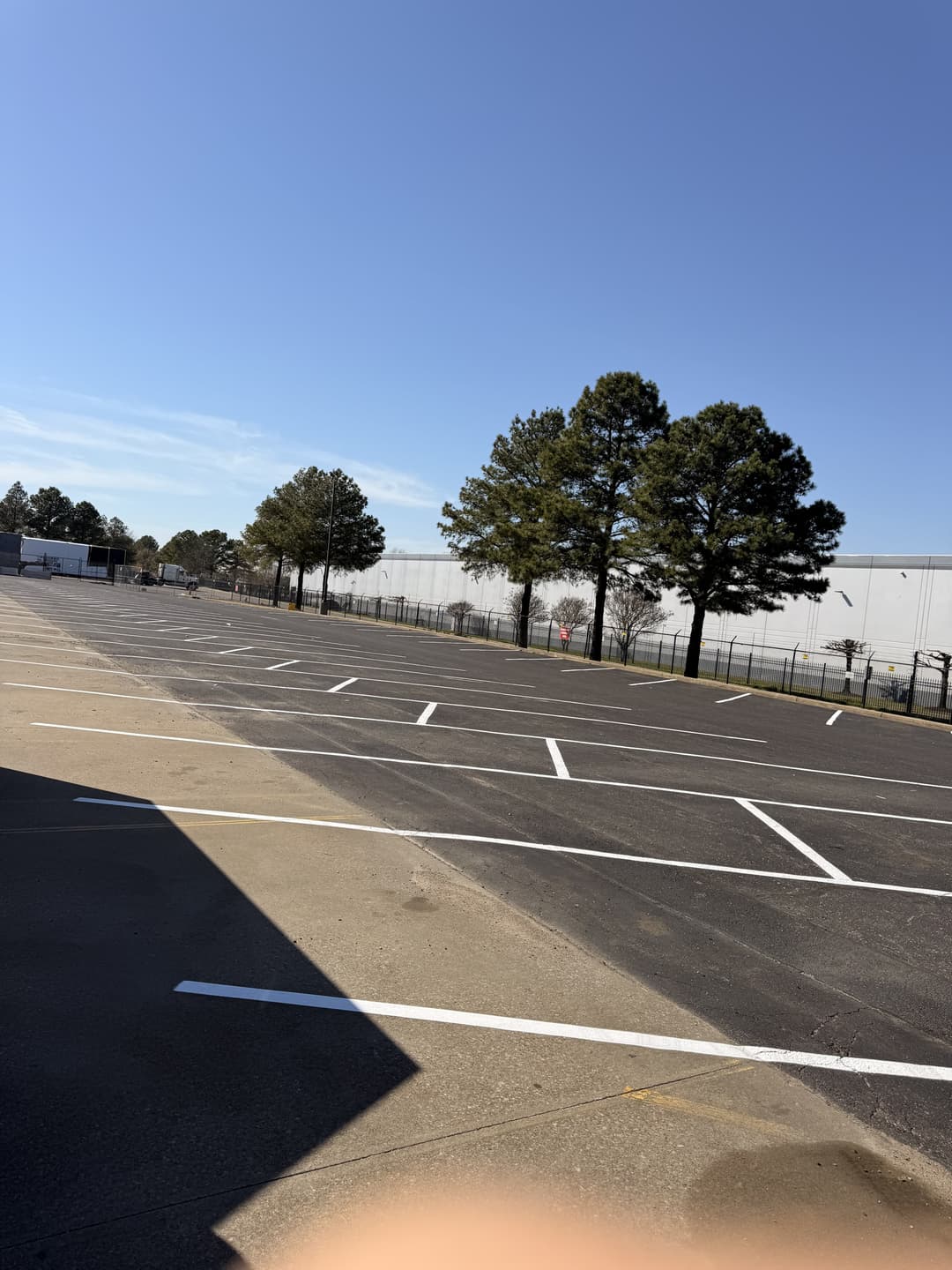 Empty parking lot with clear blue sky and trees in the background.