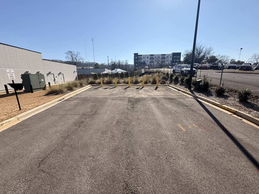 Empty parking lot with marked spaces, surrounded by grass and a building in the background.