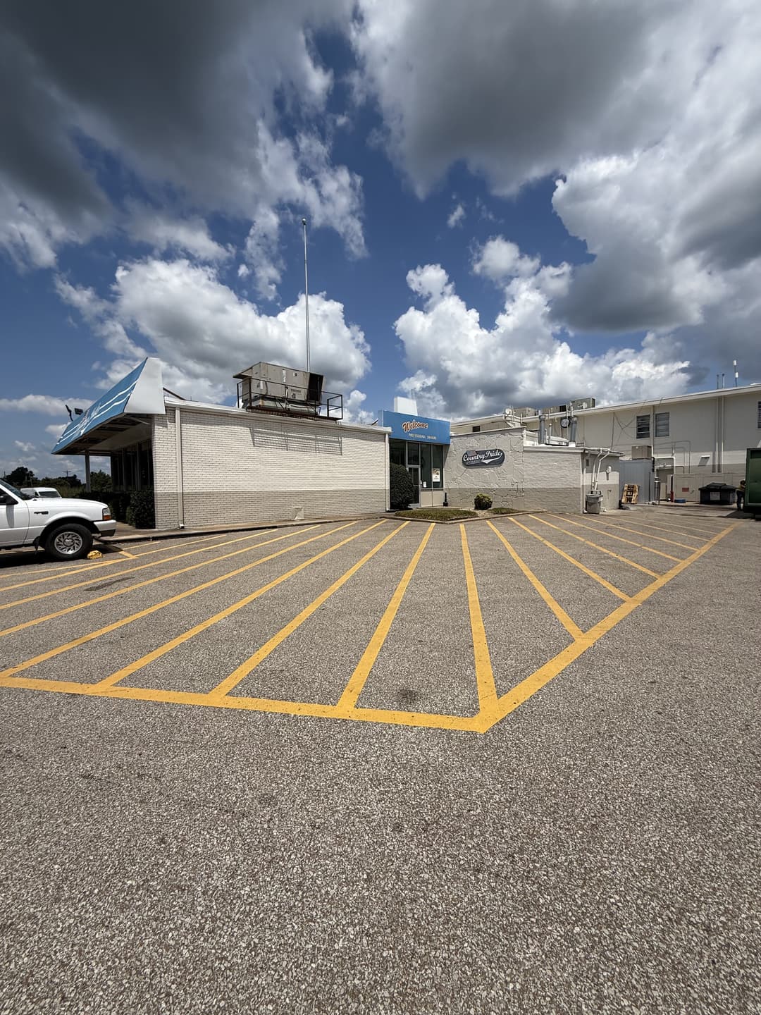 Empty parking lot with yellow stripes in front of a commercial building under a cloudy sky.
